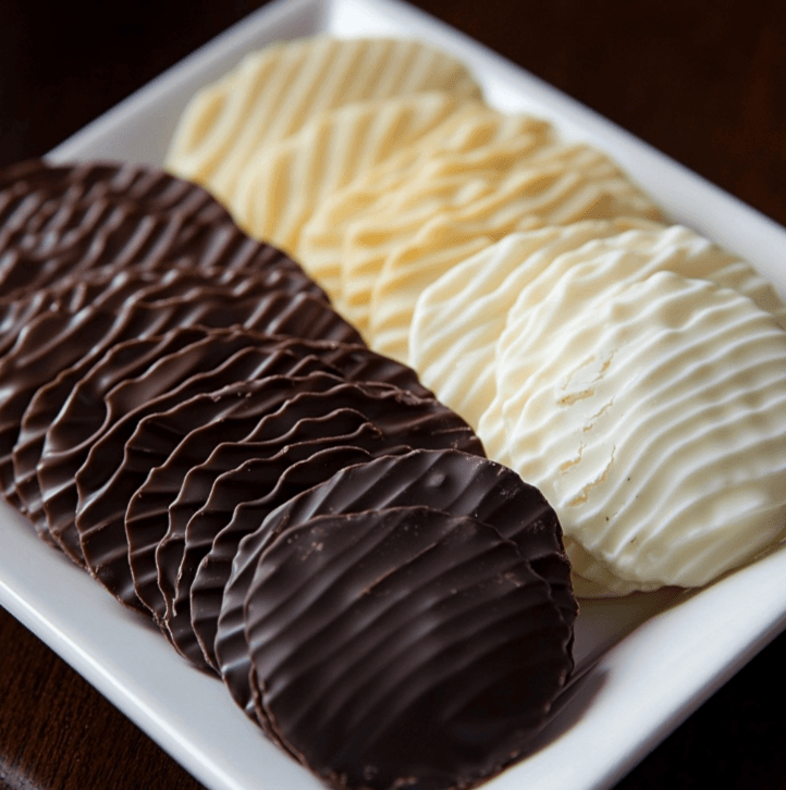 A stack of chocolate-covered potato chips on a white plate, with a bite taken out of one.