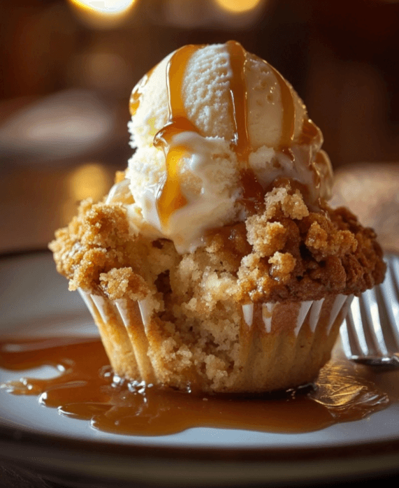  A scoop of vanilla ice cream melting over a halved apple streusel muffin, drizzled with caramel sauce